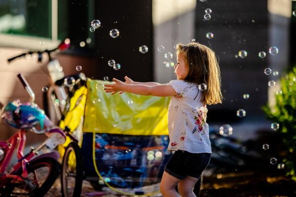 girl outside reaches for bubbles blown in air