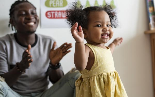Picture of girl toddler in yellow dress dancing and parent is in the background