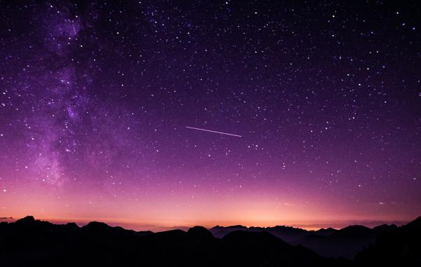 A shooting star in a purple night sky over a mountain range