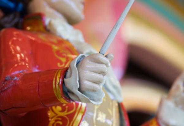 Close up of a figurine's hand as it holds a conductor wand