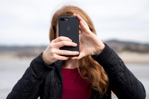a woman with red hair holds a black iphone in front of her face as though she is taking a photo of the person looking at the screen