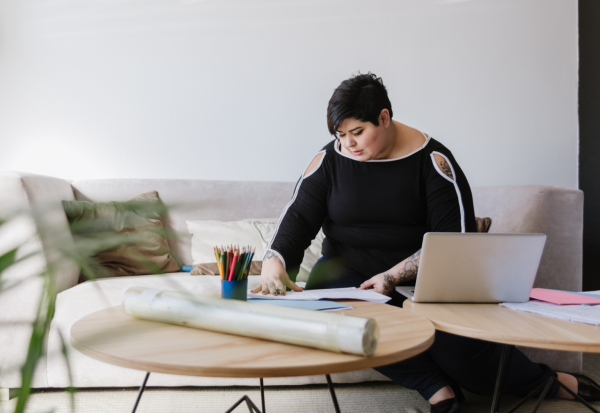 Woman working on her couch with documents and a laptop on a coffee table
