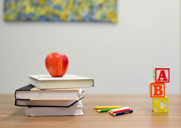 a red apple sits on top of a stack of books next to colored pencils and ABC blocks