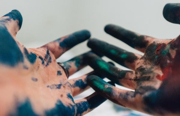Image of two open hands covered in a variety of paint colors
