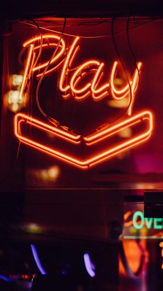An image of an orange neon sign saying "play" over an arrow towards an arcade.