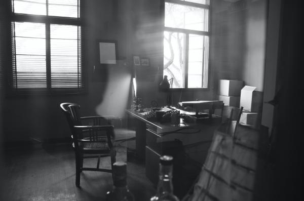 A black and white image of a messy, smoke filled detectives office.