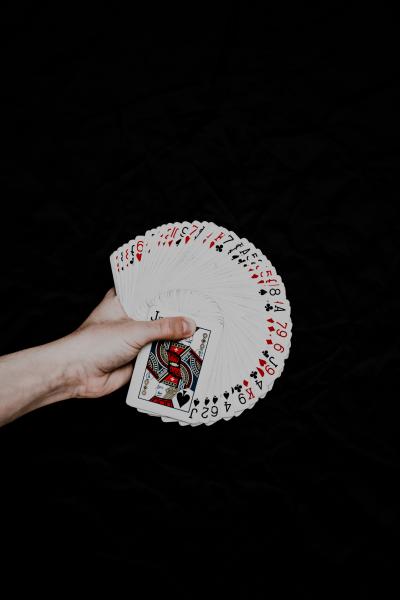 An image of a hand fanning a deck of playing cards with the faces towards the viewer in front of a black background.