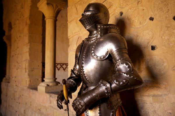 An image of a suit of medieval armor in a stone hallway.