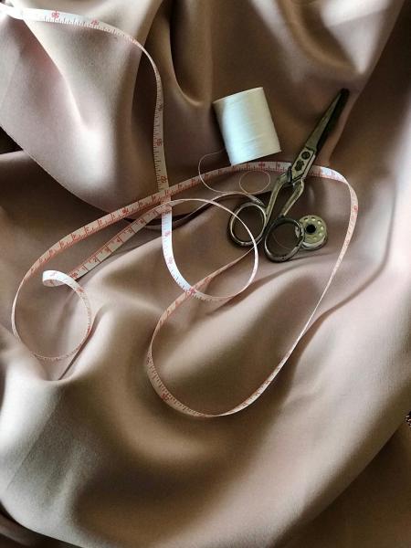 An image of beige fabric with a tape measure, thread, a bobbin, and sewing scissors resting on it.