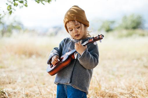 Toddler wearing a beanie playing a ukulele
