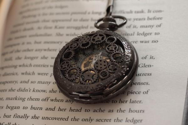 An antique pocketwatch with intricate brass details laying on a book page