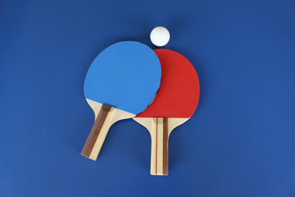 Two table tennis paddles overlapping on blue surface with table tennis ball.