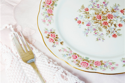 A flowery patterned plate with a lace napkin and a shiny fork on a table