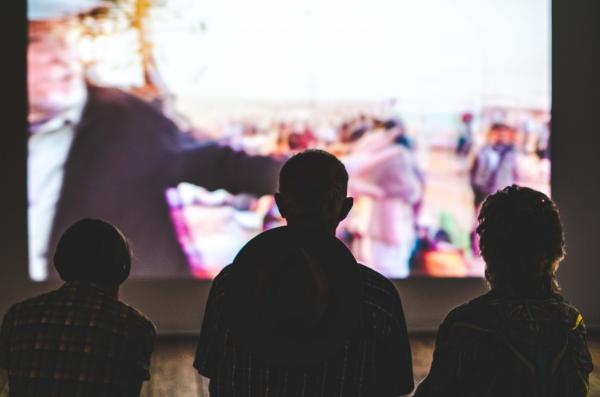 Three people watching a large movie screen.