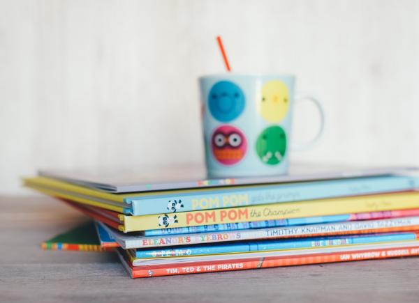 Stack of children's books with an emoji mug sitting on top.
