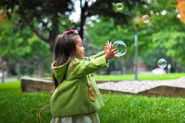 Child reaching for a bubble outside.