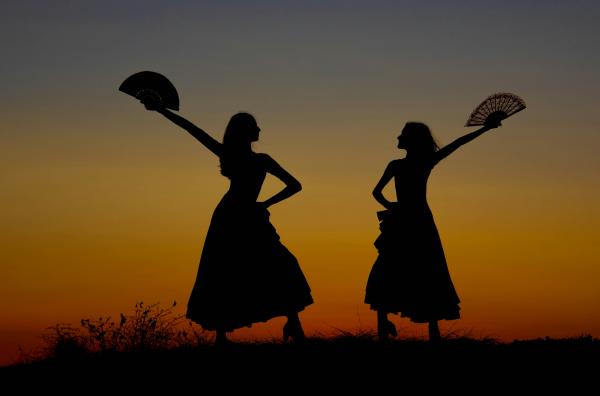 Silhouettes of two women holding fans in front of a sunset 