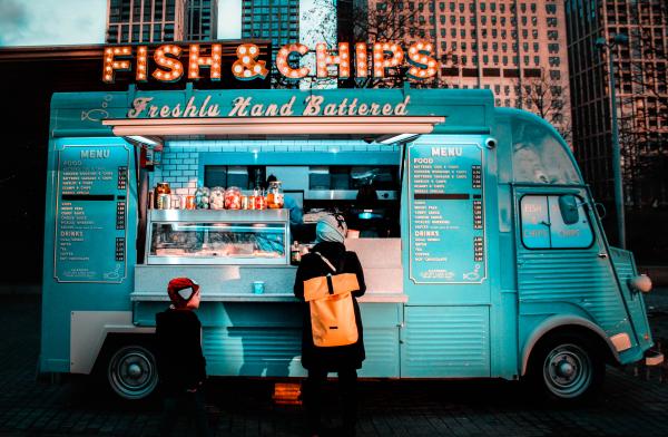 A blue food truck selling fish and chips with someone buying food at the window