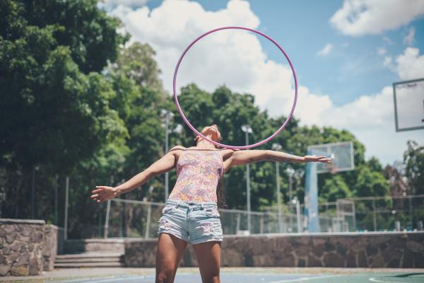 A girl dressed for summer stunting with a hula hoop on her shoulders