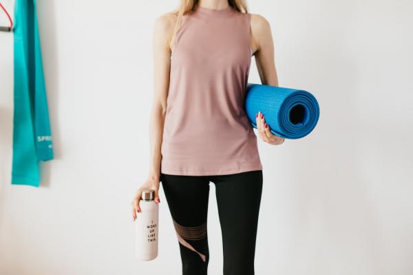 Woman in workout clothes holding a yoga mat and a water bottle