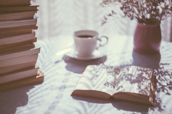 Image of an open book, dappled in sunlight, with a cup of tea behind it.