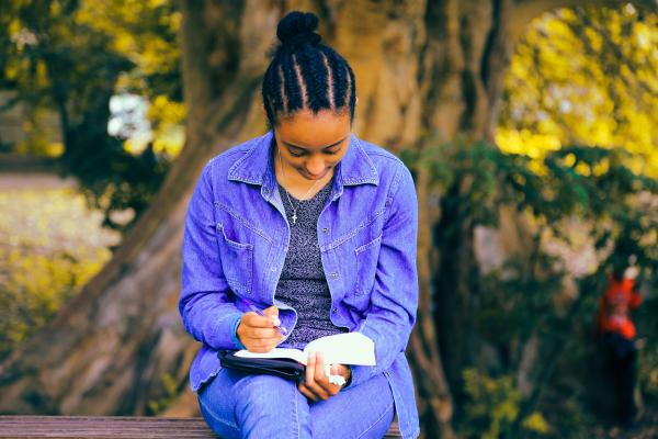 Image of teen writing in a notebook outside.