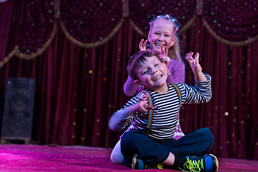 two children pretend to be monsters on a stage lit by purple light