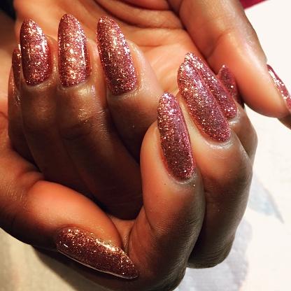 Close-up on brown-skinned woman's hands. Her nails are long, curved, and painted with red-brown glitter.