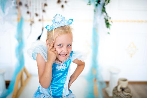 blond girl wearing a shiny blue princess dress and blue tiara, smiling at the camera