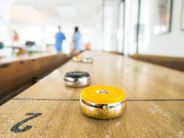 yellow shuffleboard puck in foreground on wooden board