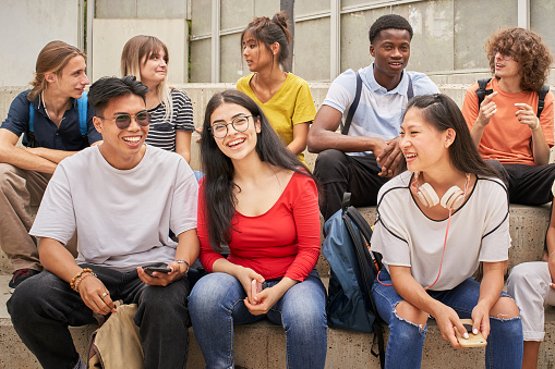 eight teens of various races and ethnicities sit in two rows, chatting and smiling
