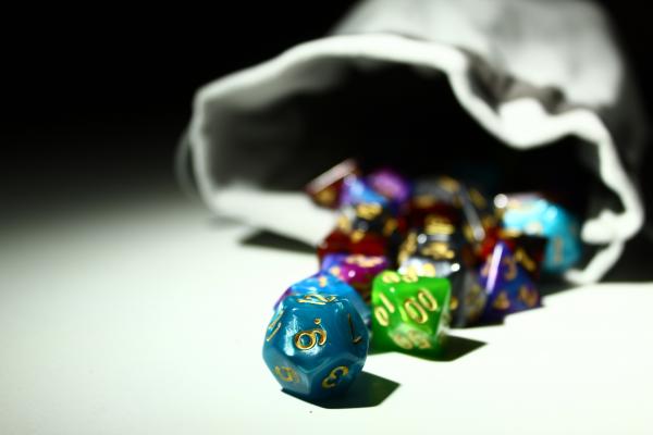 multicolored Dungeons and Dragons dice in foreground, gray bag in background
