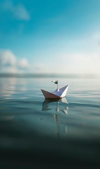 image of folded paper sailboat on open water with sky in background