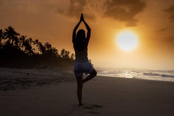 woman does yoga on a beach as the sun sets over the ocean