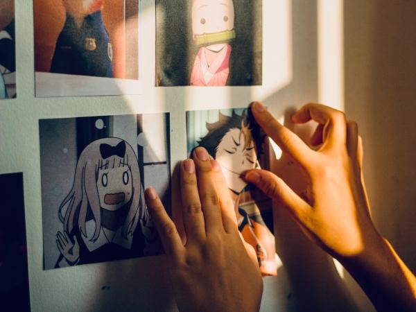 Hands adhering printouts of manga imagery to a wall