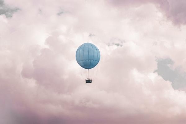 A blue orb hot air balloon floats in a cloudy sky.