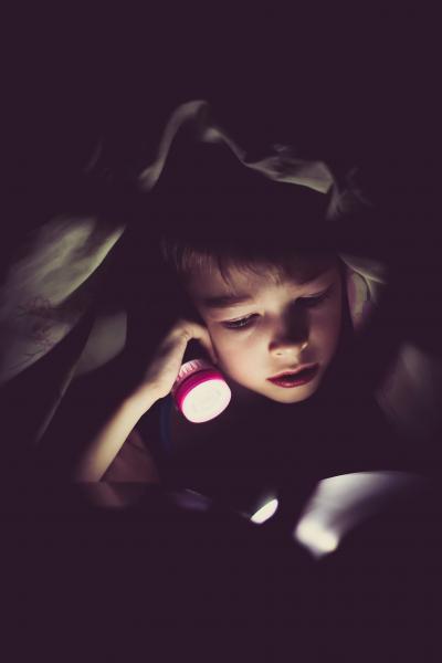 Child reading a book with a flashlight
