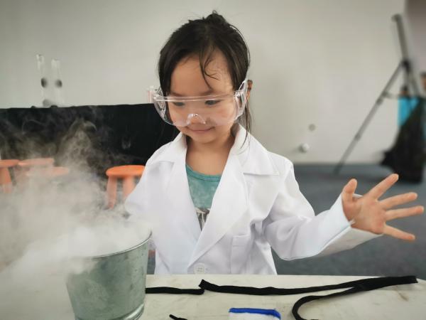 Child dressed as a scientist watching fog rise from a metal can.