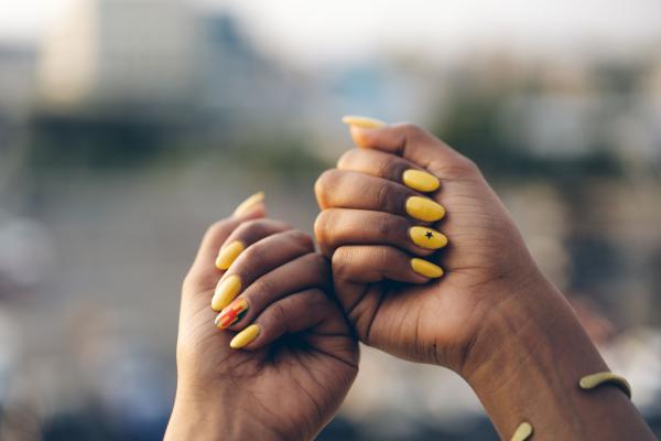 A pair of hands held up to display yellow nail art.