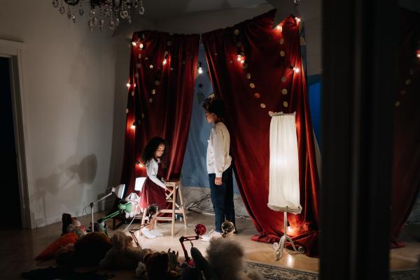 A boy and a girl acting out a play on a homemade stage with red curtains and bright lights