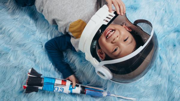 a boy wearing a toy astronaut helmet playing with a homemade rocket