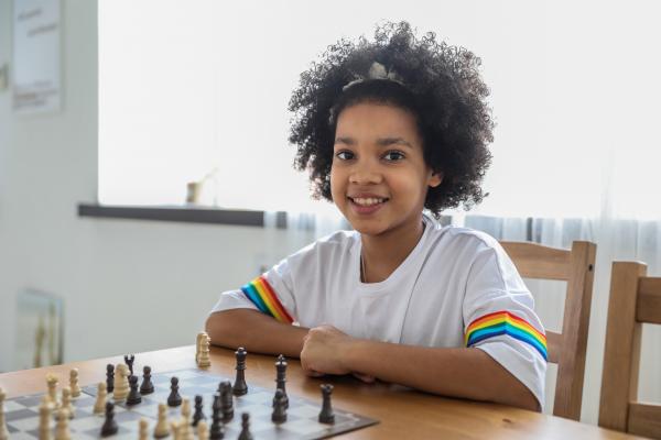 A smiling girl sitting at a table in front of a chess board