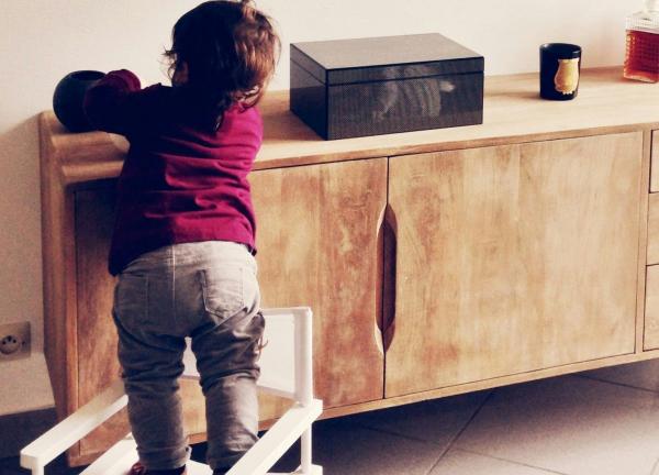 A child climbing on a chair in an unsafe way to reach something on a credenza.