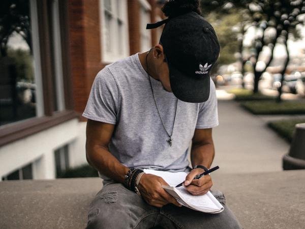 A person sitting on a wall and writing in a notebook