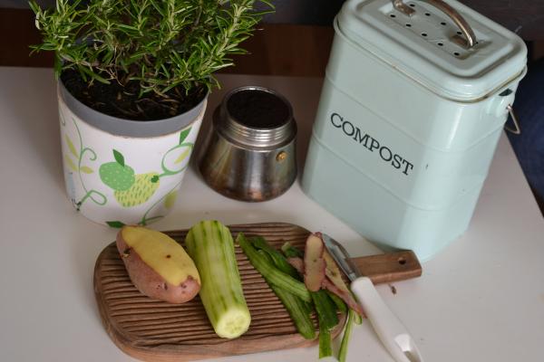 Vegetables sit on a wooden cutting board, with a compost bin next to it.